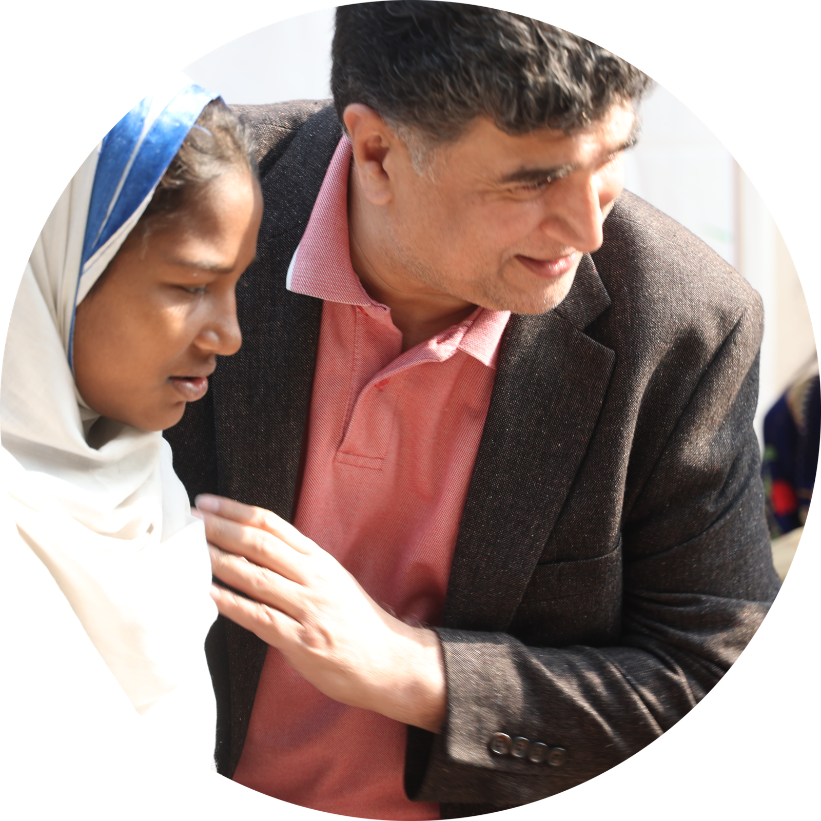 Founder Mo Azeem is sitting on his knees with Christian children at MinorCare, leaning in to listen closely to a student.