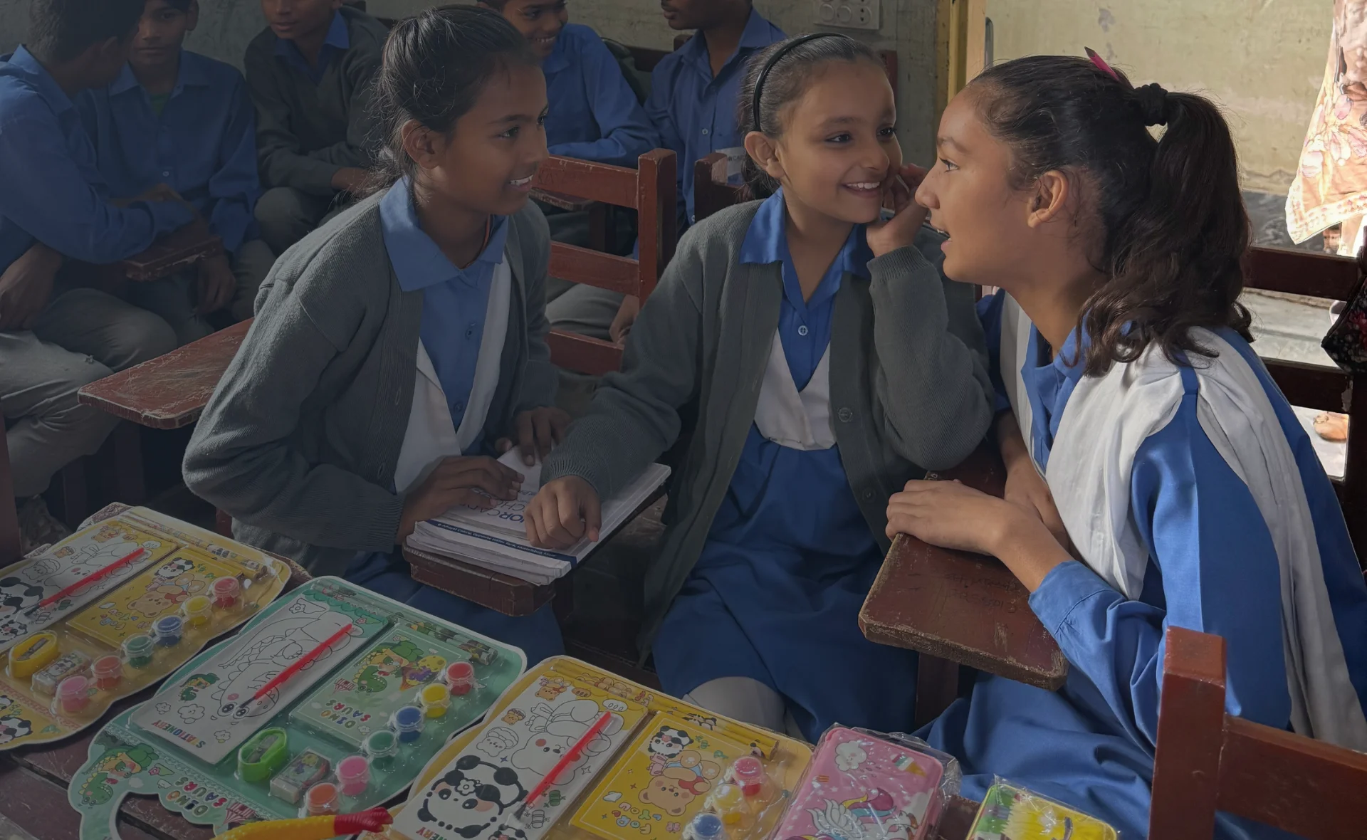 Christian children in MinorCare school uniforms sitting at their desks and talking to each other inside the classroom.
