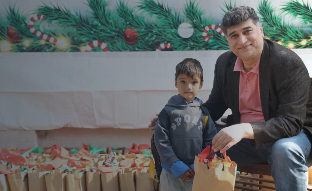 Founder Mo Azeem sitting on his knees with a very young Christian student at MinorCare, engaging with care and warmth.