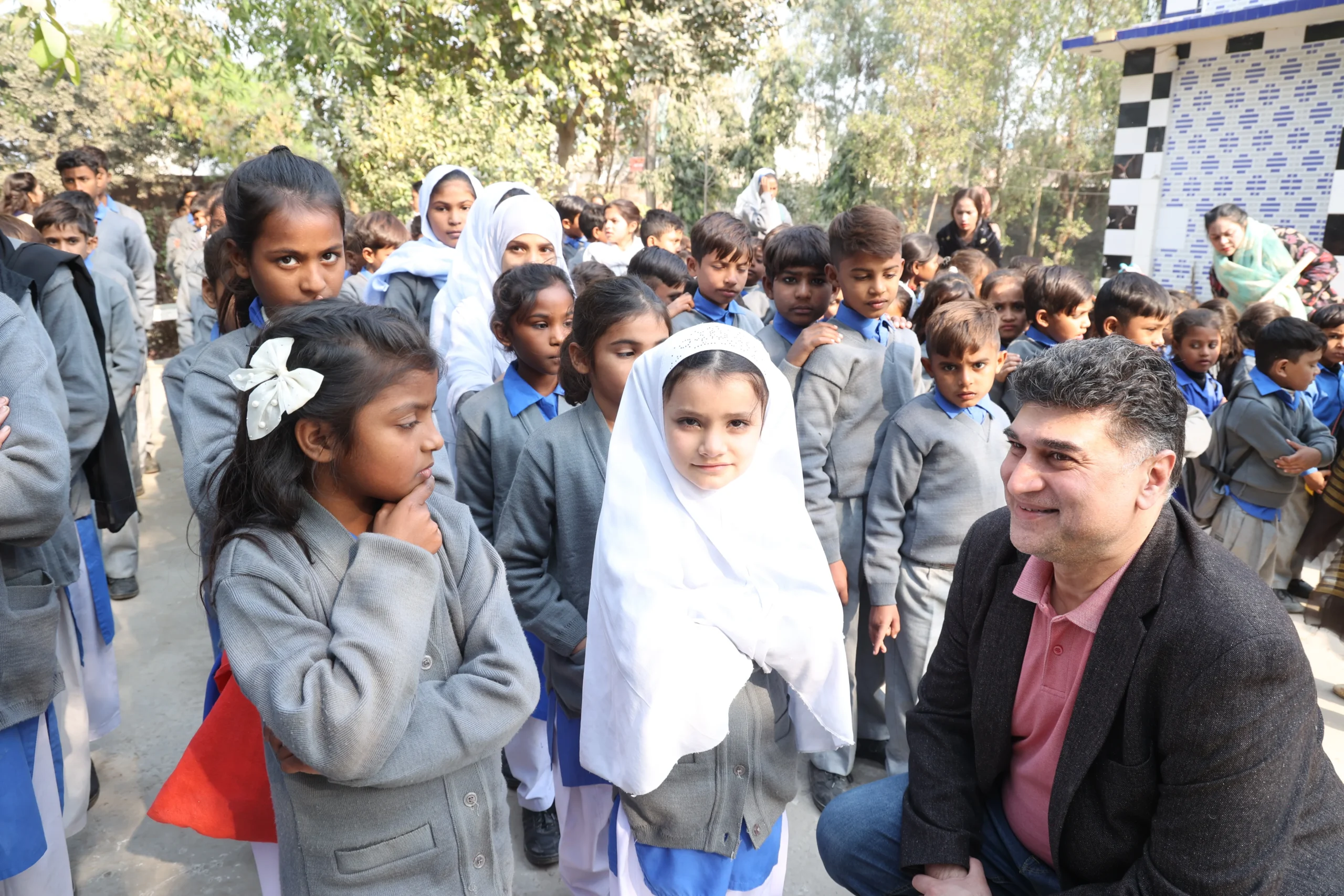 Founder Mo Azeem is sitting on his knees with Christian children at MinorCare, leaning in to listen closely to a student.