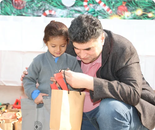 Founder Mo Azeem sitting on his knees with Christian children at MinorCare, listening attentively to a young student.